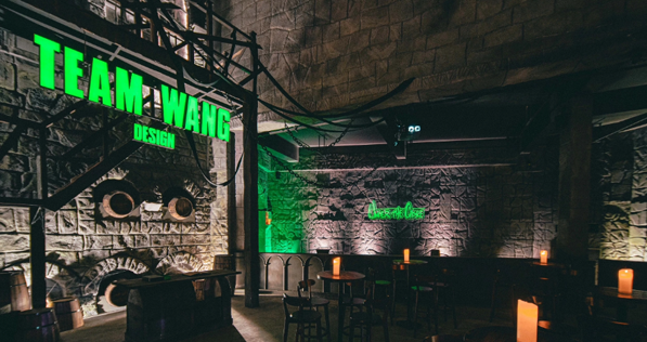 Stone castle exhibition interior with glowing green TEAM WANG DESIGN signage