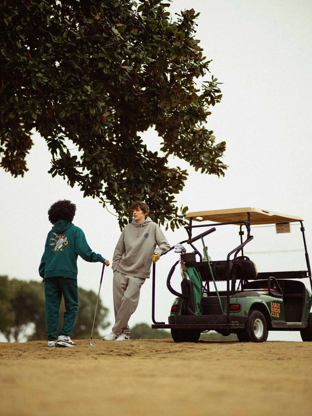 Two models and a golf cart beneath a tree on the course